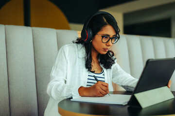 Focused college student wearing headphones working on an assignment with a tablet