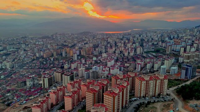 The video shows a wide cityscape at sunset with completed multi-story residential buildings in the foreground. The housing appears to be part of a large-scale residential construction project.