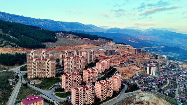 The video shows a multi-story residential construction site. Buildings are at different stages; some in the rough construction phase. The site includes roads, material areas,situated on a hillside.