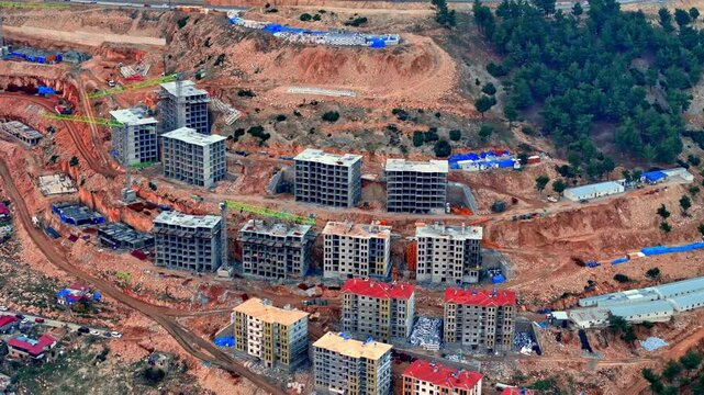 The video shows a multi-story residential construction site. Buildings are at different stages; some in the rough construction phase. The site includes roads, material areas,situated on a hillside.