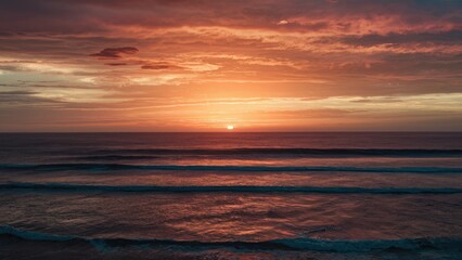 Fototapeta premium Tranquil ocean sunrise with orange and pink hues blending into clouds above calm waves, reflecting serene light across the water.