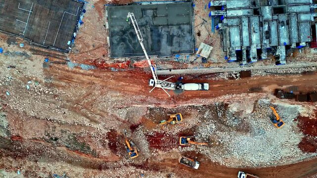 The video shows a residential construction site with concrete blocks, foundation work, and ground preparation in progress. Machinery, including a crane and concrete pump, is actively operating.