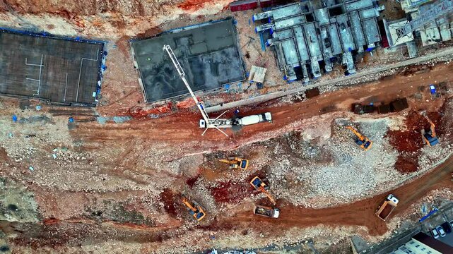 The video shows a residential construction site with concrete blocks, foundation work, and ground preparation in progress. Machinery, including a crane and concrete pump, is actively operating.