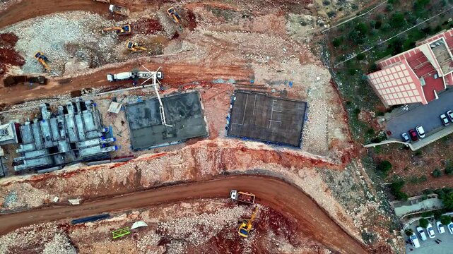 The video shows a residential construction site with concrete blocks, foundation work, and ground preparation in progress. Machinery, including a crane and concrete pump, is actively operating.