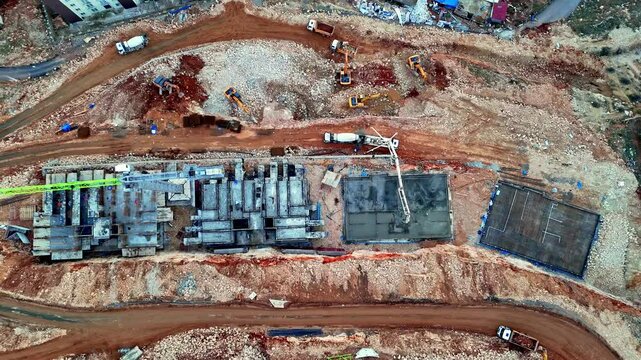The video shows a residential construction site with concrete blocks, foundation work, and ground preparation in progress. Machinery, including a crane and concrete pump, is actively operating.