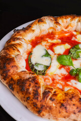 Pizza tradizionale napoletana margherita con sugo di pomodoro, mozzarella e basilico fresco con il cornicione ripieno di ricotta e speck