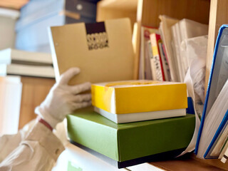 箱などが前にある本棚からスクラップブックを取り出す手元