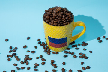 Top view of glass with Colombian flag filled with coffee beans on a light blue background, Colombian culture and coffee concept