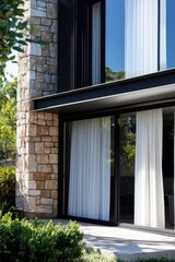 Fototapeta premium Modern architectural design featuring a stone facade and large glass windows in a tranquil outdoor setting during daytime
