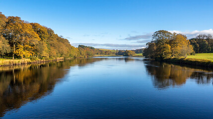 Scenic view of a tranquil river surrounded by autumn foliage under a clear blue sky