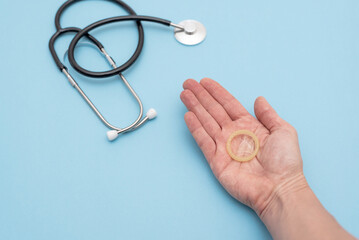 Hand holding a condom promoting safe sex and contraception near a stethoscope on a blue background