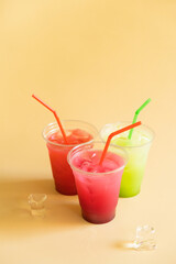 Colored summer lemonades with straws and ice on a beige background