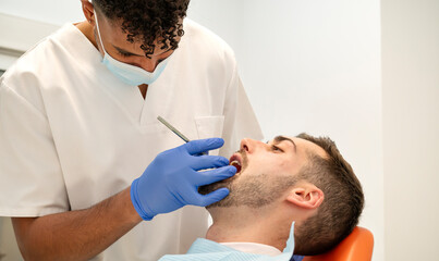 Fototapeta premium Dentist carefully performing a routine oral examination and treatment on a male patient in a modern and clean dental clinic