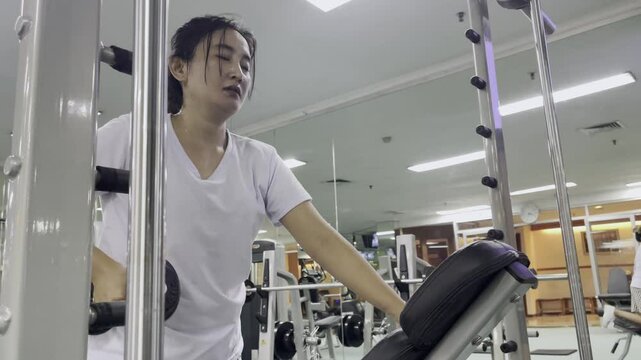 A woman is working out at the gym. She is lifting a dumbbell. She is wearing a white shirt and black and white pants. She is sweating and focused on her workout.