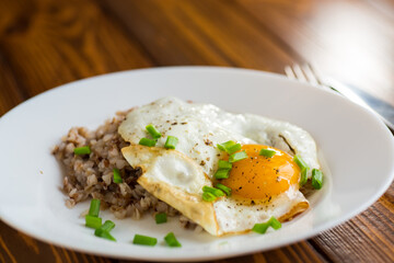 Fried eggs with boiled buckwheat and onions on a wooden table