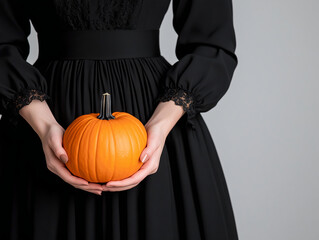 Minimalist Halloween scene featuring a traditional pumpkin held by hands in black attire.