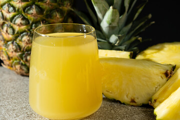 Pineapple juice in a glass among fresh pineapple fruit close-up.