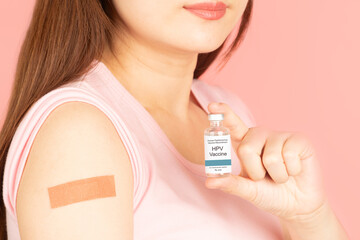 International HPV awareness day concept. Happy woman showing vaccinated arm with medical adhesive bandage strip after HPV vaccine injection over pink background.