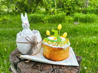easter cake with easter eggs and bunny. Easter cake with colorful decorations and a ceramic bunny in an egg. The composition is set on a tree stump in a lush green garden