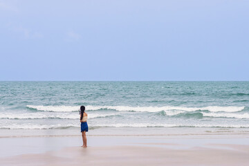 Back view of happy carefree woman using mobile phone at beach. Woman using smartphone standing at beach. Beautiful lovely young woman spending time at beach. Concept of travel, tourism and vacation.