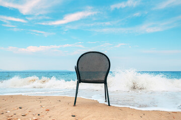 Empty metallic chair on sandy beach in Vrasna Greece. Aegean sea waves splashing the sand shoreline...