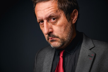 Portrait of mature adult entrepreneur with forehead wrinkles in elegant gray suit with black shirt...