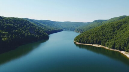 Fototapeta premium Aerial view of a serene blue lake surrounded by lush green mountains on a clear day