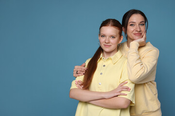 Fototapeta premium Portrait of beautiful mother with teenage daughter on light blue background, space for text