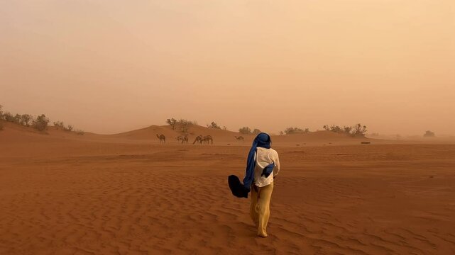Berber Arab man walking in large desert with camel landscape in background