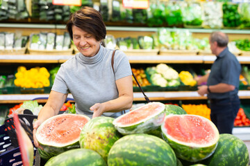 Elderly woman chooses watermelon in fruit and vegetable section