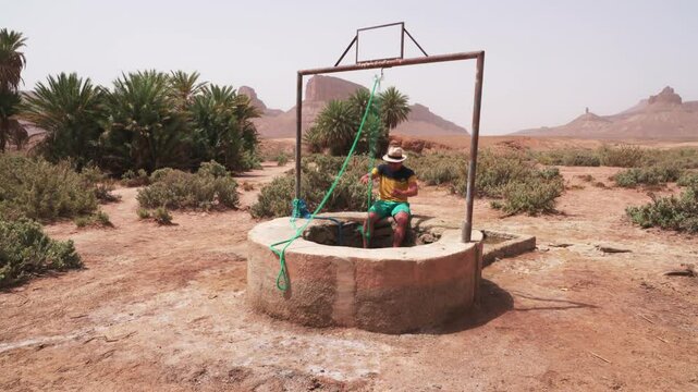 Man drawing water from a deep well or cistern in the middle of an oasis landscape in the desert