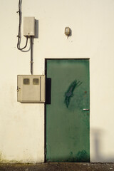 Puerta metálica en fachada blanca con cables y cajas de registro