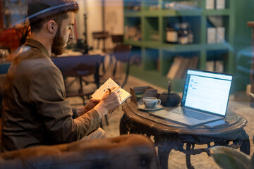 Man writing notes in notebook seen through cafe window reflections