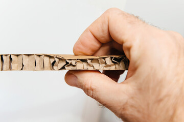 Fototapeta premium A hand holding a section of corrugated cardboard showcasing its layered structure with folds and spaces for added strength and flexibility