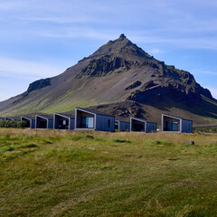 Modern tourist cabins with panoramic mountain views in Iceland. Minimalist architecture seamlessly integrated into the natural landscape beneath a distinctive peak.