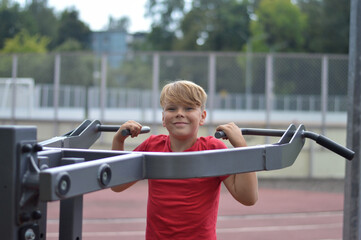 Little boy working out in nature park, using cross trainer in outdoor gym.