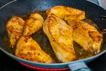 Cooking seasoned chicken fillets in a frying pan on a stove at home
