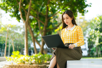A young woman works on laptop outdoors, surrounded by greenery and sunlight. Digital Nomad Lifestyle Freelance Hybrid Work communicating with a colleague