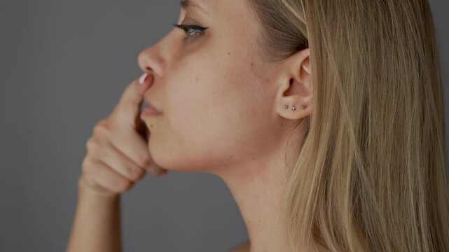 Young woman standing in profile showing her perfect nose after rhinoplasty on dark grey background. The result of cosmetic plastic surgery on the hump of female nose. Correction of the nasal septum