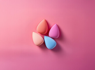 Fototapeta premium Four pastel-colored teardrop makeup sponges arranged on a pink background. Clean, simple, and aesthetically pleasing.