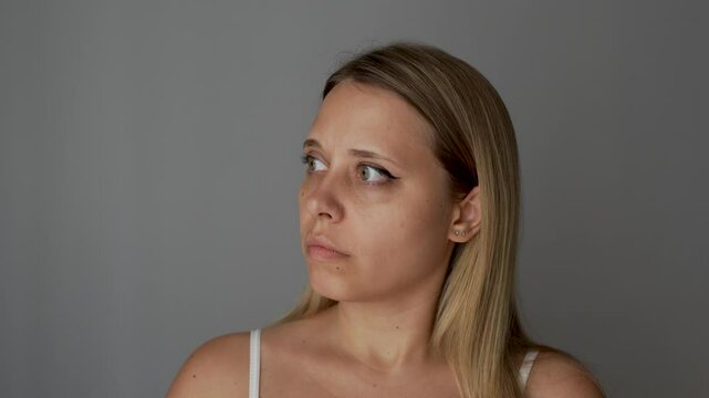 Young blonde woman opens her eyes wide, startled by the sudden noise on a dark grey background. Sudden reaction to an external stimulus, neurosis, misophobia, fear, fright. Highly sensitive person