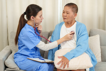 Obraz premium Nurse using stethoscope to check heartbeat of elderly Asian woman during rehabilitation session at home. Nurse demonstrating professional care and attention in a supportive environment.