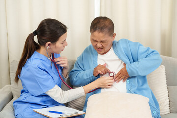 Obraz premium Nurse performing chest examination with stethoscope on elderly Asian woman experiencing discomfort during recovery. Home healthcare session providing focused and compassionate care.
