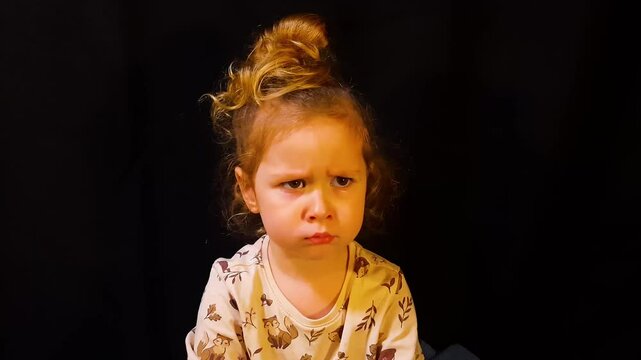 Little girl on a black background is angry