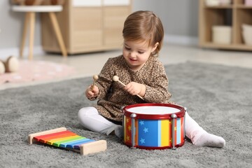 Cute little girl playing with toy musical instruments on floor at home