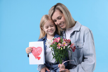 Little daughter congratulating her mom with bouquet of alstroemeria flowers and greeting card on light blue background. Happy Mother's Day