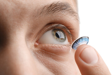 Man putting color contact lens in his eye on white background, closeup