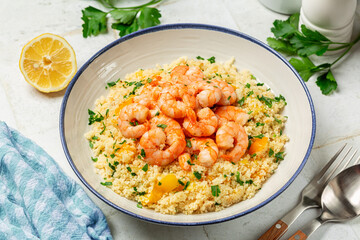 A plate with Couscous and fried Shrimps, yellow tomatoes, onion, parsley. White table surface, blue napkin.