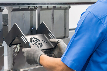 Close up the bending machine operator hold the sheet metal parts with rubber glove.