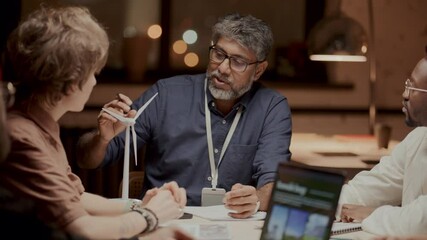 Senior male engineer explaining wind turbine model to diverse team during discussion on renewable energy solutions at office meeting - Powered by Adobe